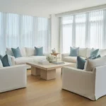 Elegant coastal living room with white sofas, blue pillows, and natural light