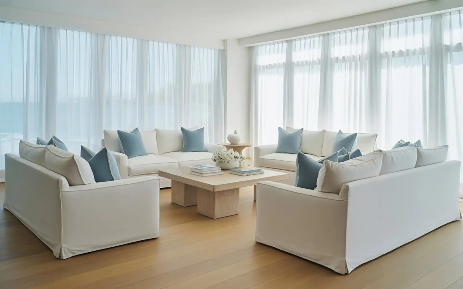Elegant coastal living room with white sofas, blue pillows, and natural light